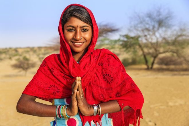 namaste--portrait-of-happy-indian-girl-in-desert-village--india-622457258-5a60ca9f7d4be80037c93e52